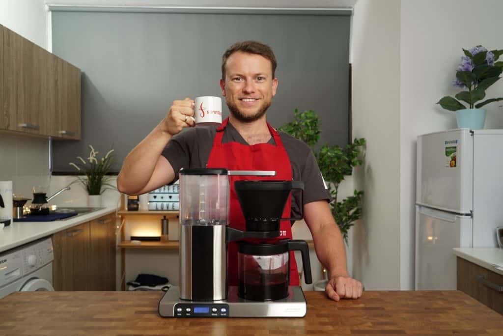 Barista Arne steht hinter der Gastroback Design Brew Advanced Kaffeemaschine mit einer Tasse in der rechten Hand