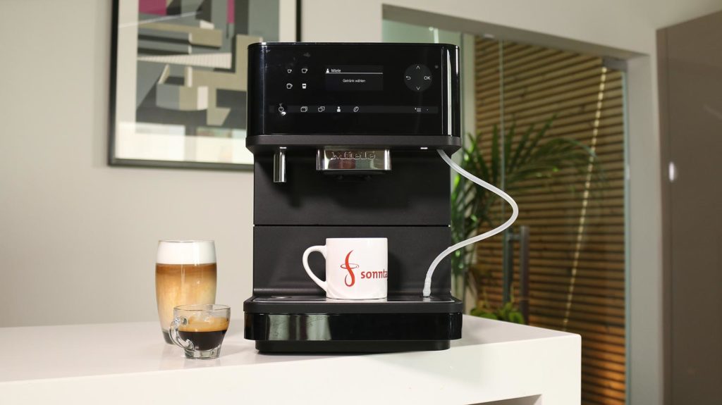 Miele CM 6350 - Gesamtansicht des Kaffeevollautomaten mit einem Latte Macchiato und Espresso links daneben