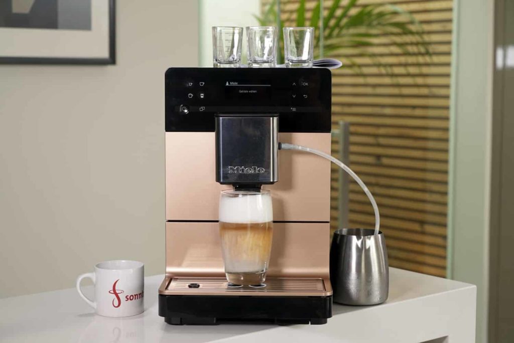 Ein Latte Macchiato mit sehr hoher Milchschaumkrone steht unter der Auslaufdüse des Miele CM 5500