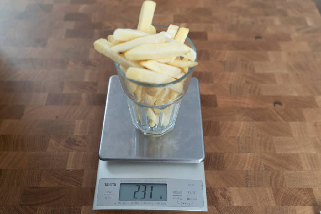 Pommes Frites werden in einem Glas auf einer Digitalwaage abgewogen